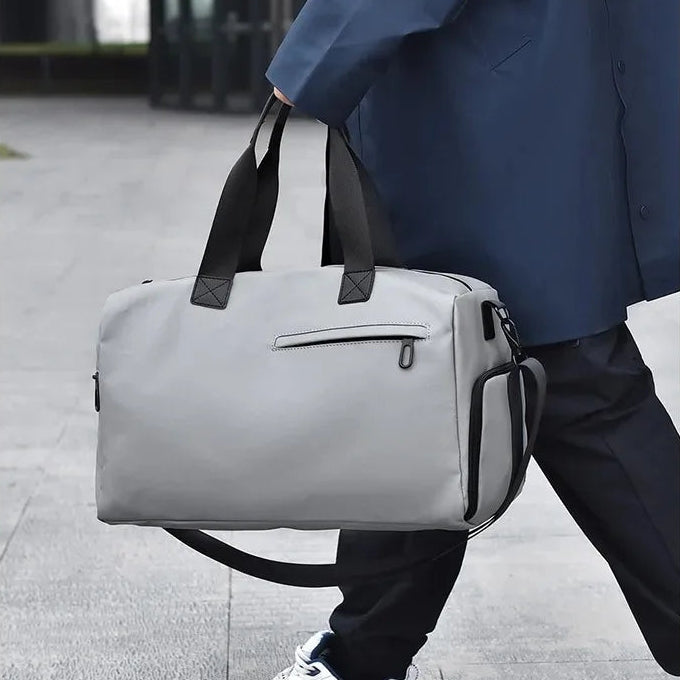 Gray duffel bag with black straps, carried by person in urban setting, minimalist design for commuters