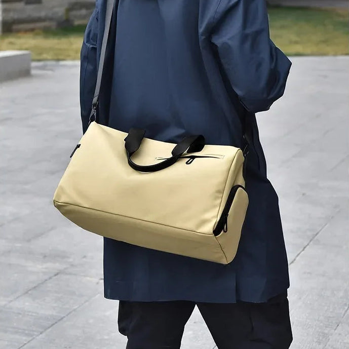 Beige duffel bag with black handles, worn crossbody by person in blue coat, urban commuter style