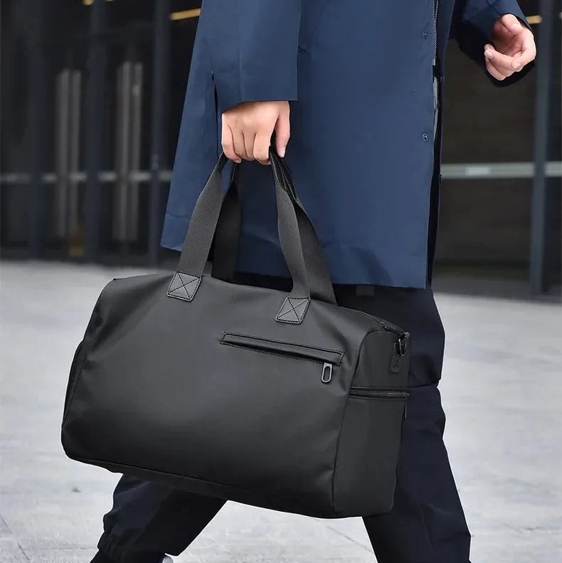 Black minimalist travel duffel bag with top handles, carried by commuter in urban setting